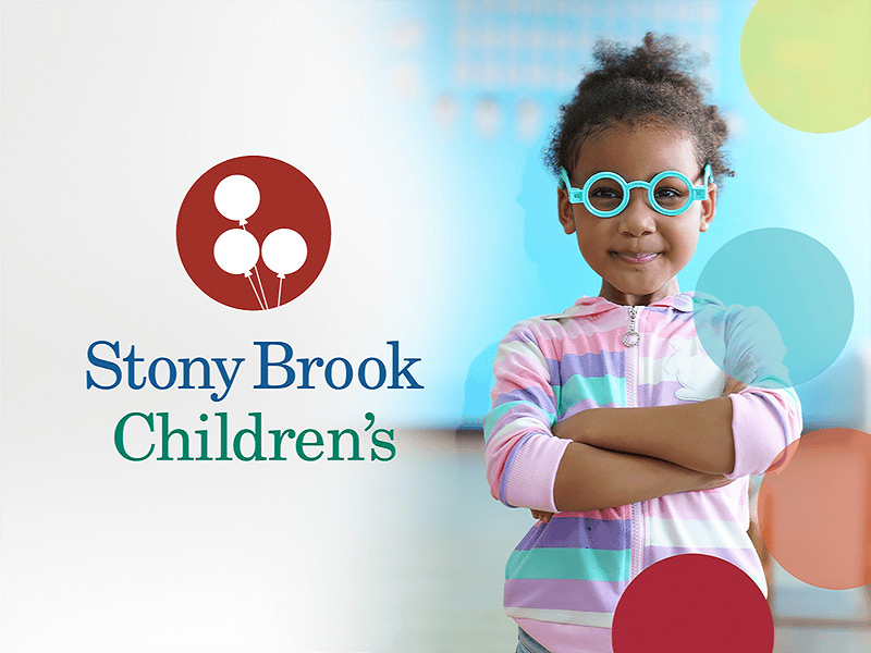 Stony Brook Children’s logo with three white balloons next to a smiling young girl wearing colorful glasses and a striped hoodie, standing with arms crossed.