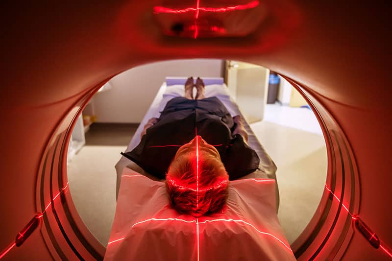 Patient lying in an MRI machine with red laser positioning lights projected on their head.