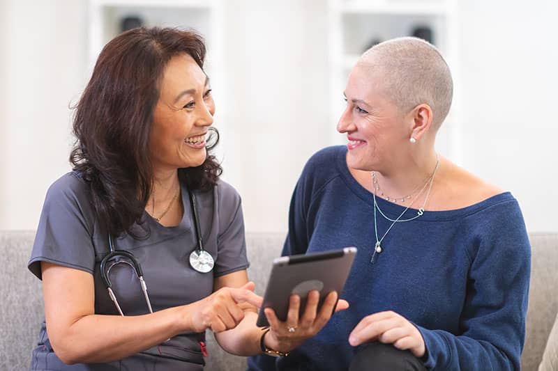 Healthcare professional showing a tablet to a smiling cancer patient with a shaved head.