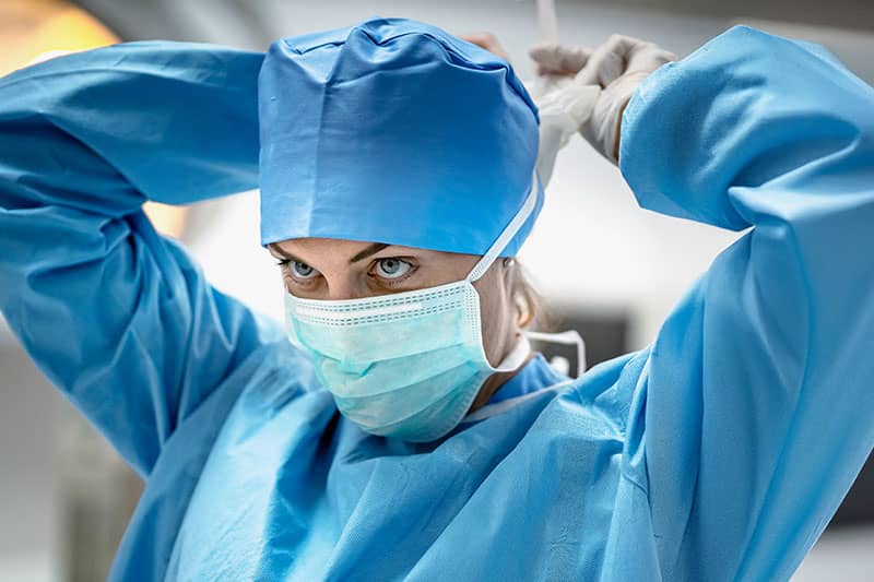 Focused surgeon adjusting her cap and face mask while preparing for surgery in a sterile environment.